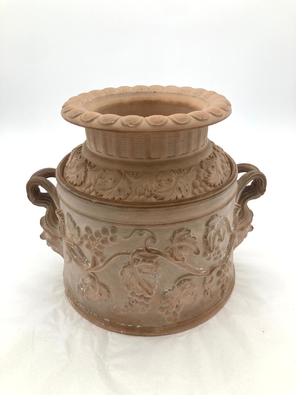 An unglazed terracotta wine cooler featuring twin scroll handles, a basketweave collar, and relief-moulded grape and vine leaf motifs.