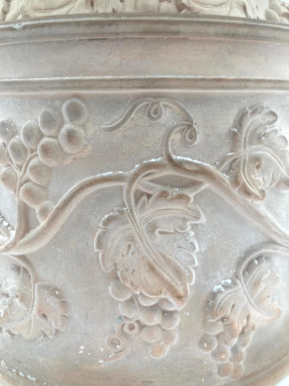 An unglazed terracotta wine cooler featuring twin scroll handles, a basketweave collar, and relief-moulded grape and vine leaf motifs. View V