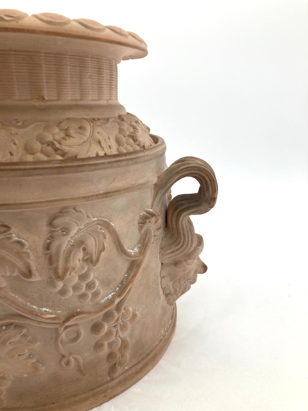 An unglazed terracotta wine cooler featuring twin scroll handles, a basketweave collar, and relief-moulded grape and vine leaf motifs. View X