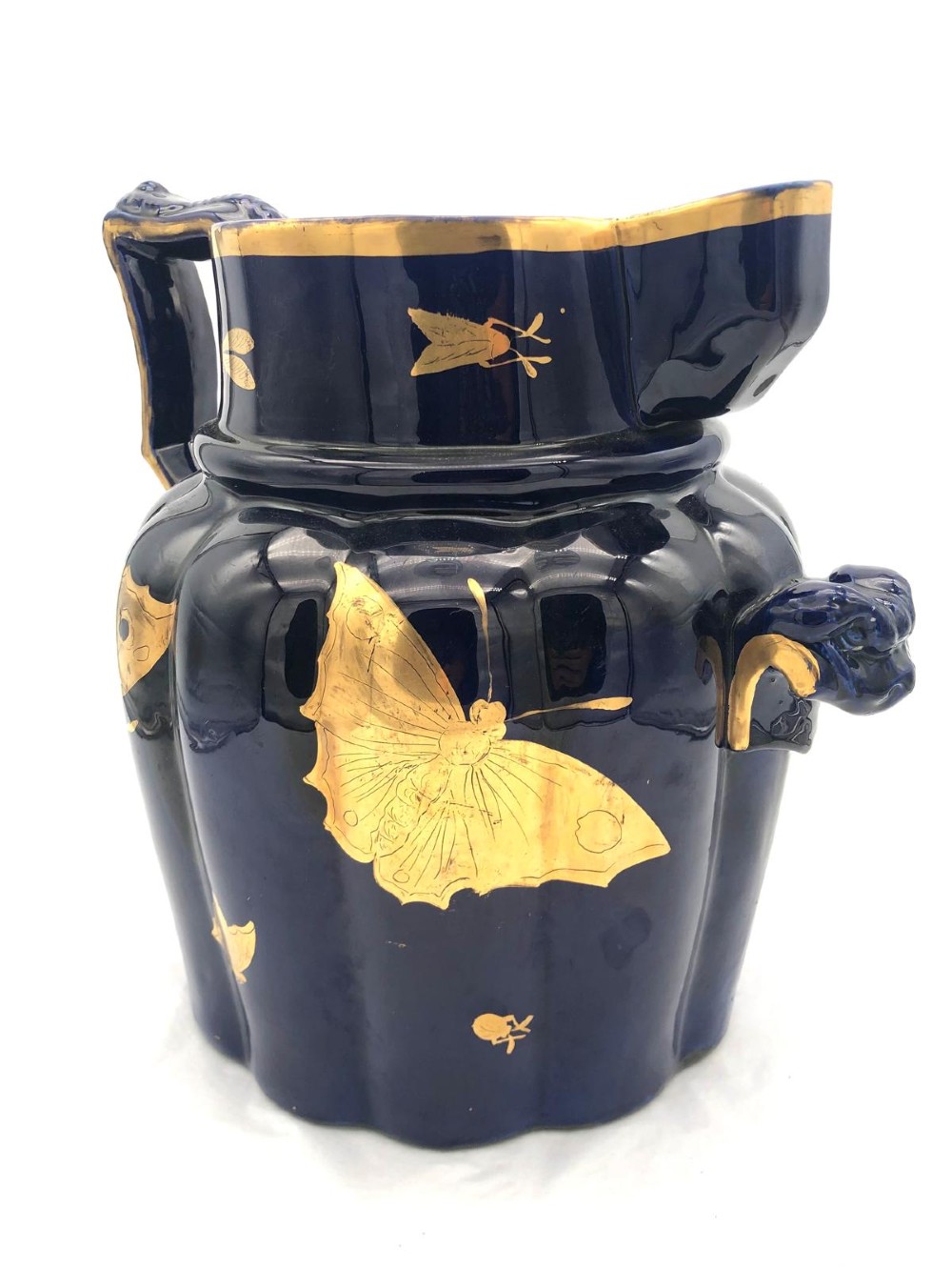 A deep cobalt blue porcelain jug decorated with gilded butterfly motifs and a wide spout, dating to circa 1820.