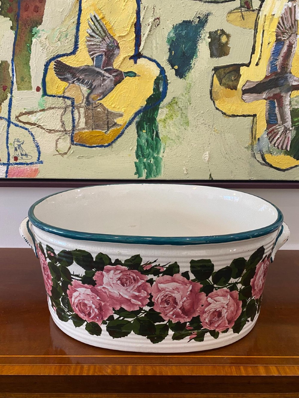 An oval white glazed ceramic footbath decorated with hand-painted pink cabbage roses, green foliage, a green painted rim, and twin side handles.