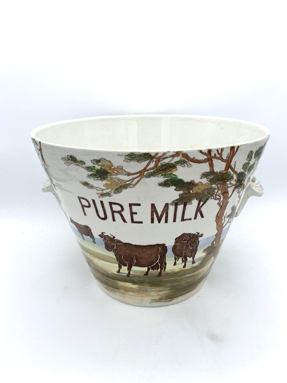 A cream earthenware Victorian milk pail decorated with brown painted cows under trees and lettering stating Pure Milk.