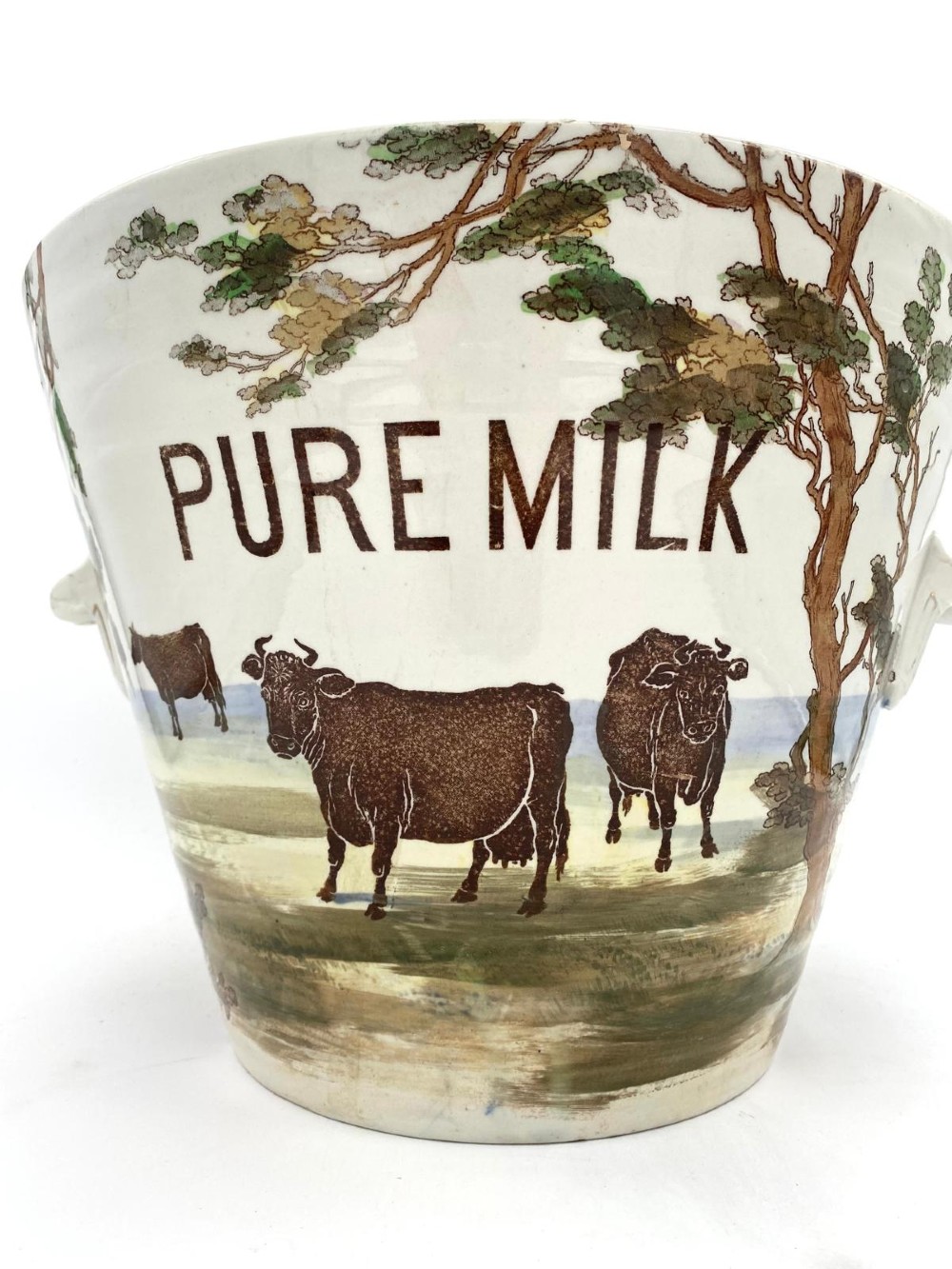A cream earthenware Victorian milk pail decorated with brown painted cows under trees and lettering stating Pure Milk. View III