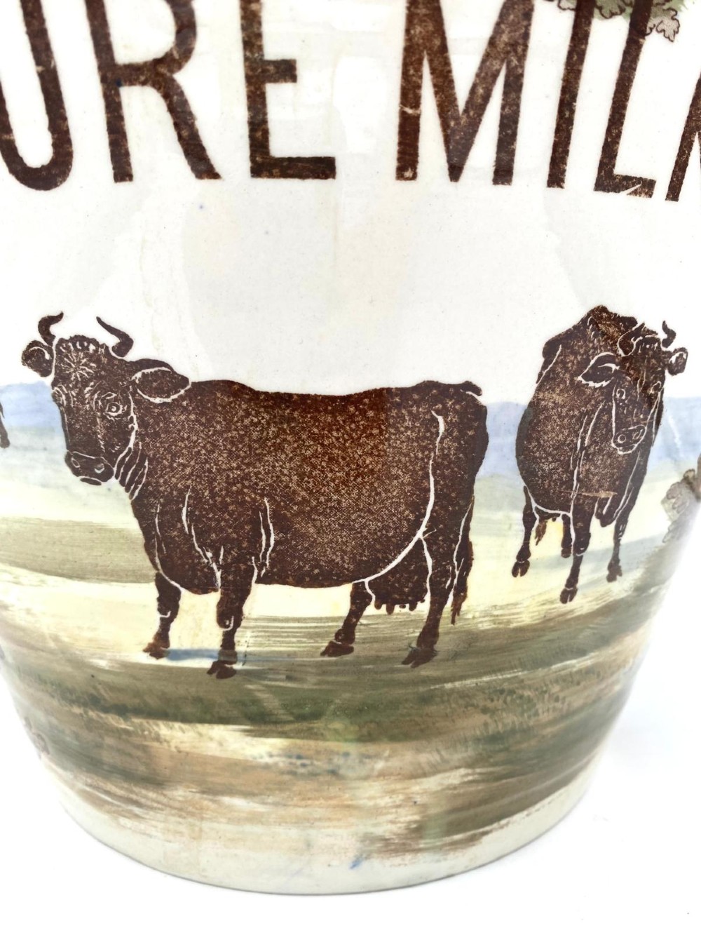 A cream earthenware Victorian milk pail decorated with brown painted cows under trees and lettering stating Pure Milk. View IV