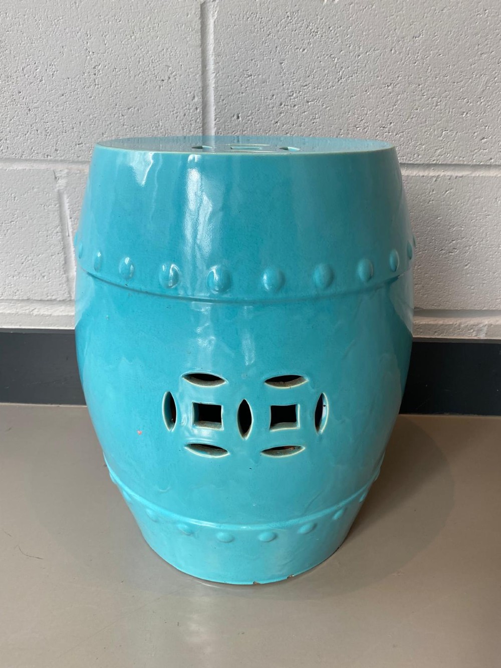 A vibrant turquoise glazed majolica ceramic barrel-shaped garden seat with raised stud detailing and pierced geometric openings.