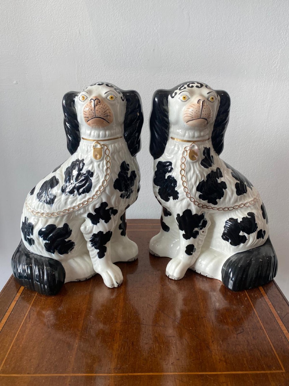 A pair of moulded white glazed ceramic Staffordshire spaniels decorated with hand-painted black patches, yellow eyes, and gilded chain collars.