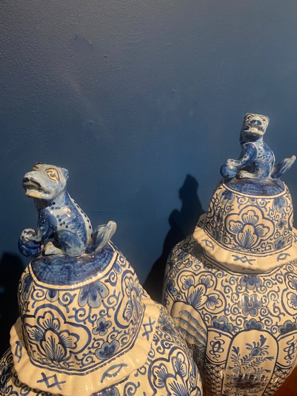 A pair of mid-19th century ribbed blue and white tin-glazed earthenware lidded vases hand-painted with oriental landscapes and topped with seated lion finials. View II