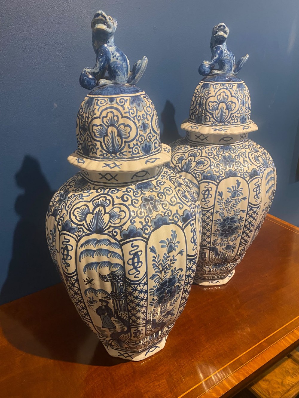 A pair of mid-19th century ribbed blue and white tin-glazed earthenware lidded vases hand-painted with oriental landscapes and topped with seated lion finials. View III