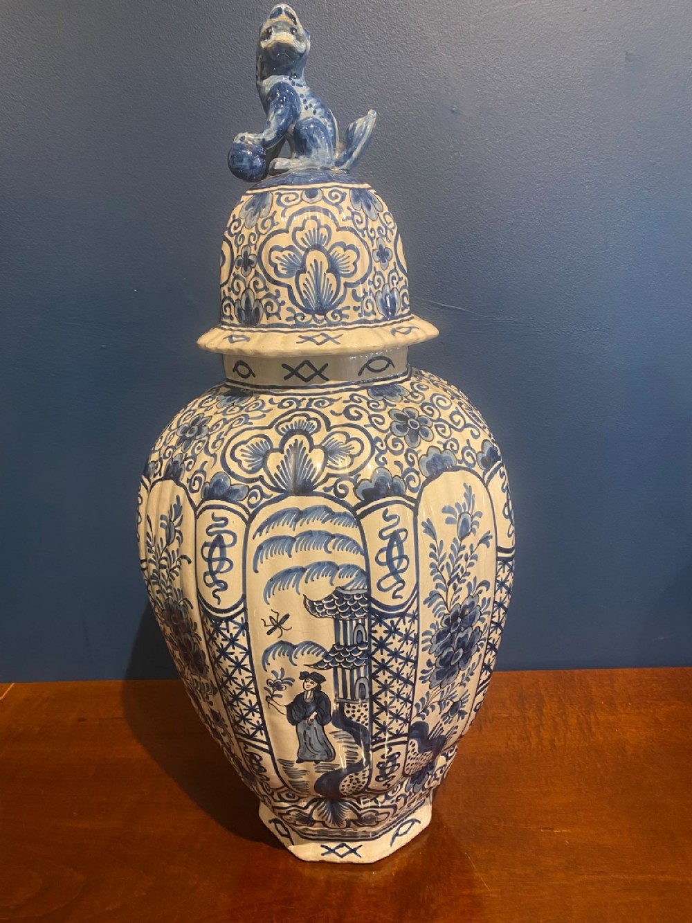 A pair of mid-19th century ribbed blue and white tin-glazed earthenware lidded vases hand-painted with oriental landscapes and topped with seated lion finials. View IV