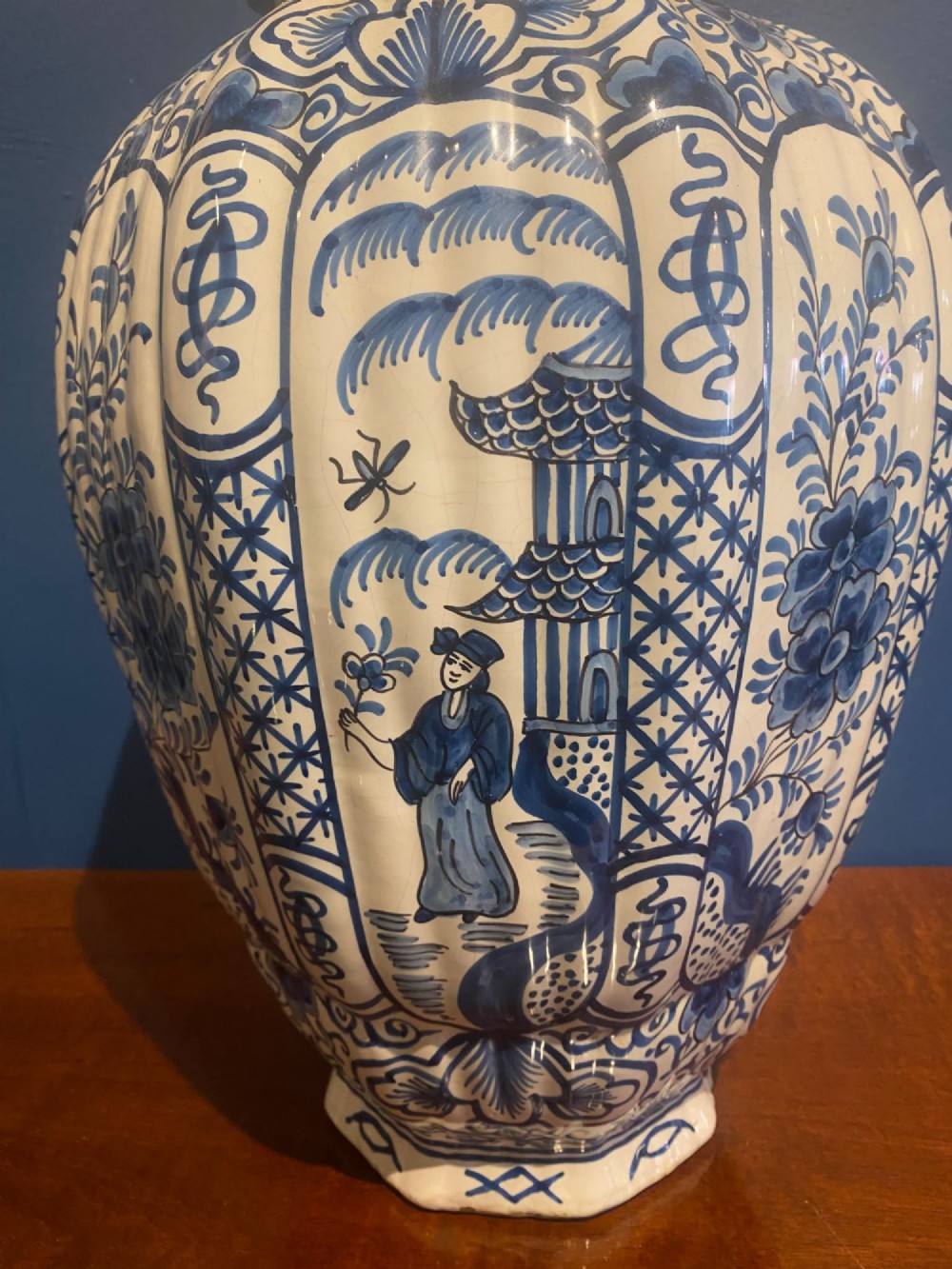 A pair of mid-19th century ribbed blue and white tin-glazed earthenware lidded vases hand-painted with oriental landscapes and topped with seated lion finials. View V