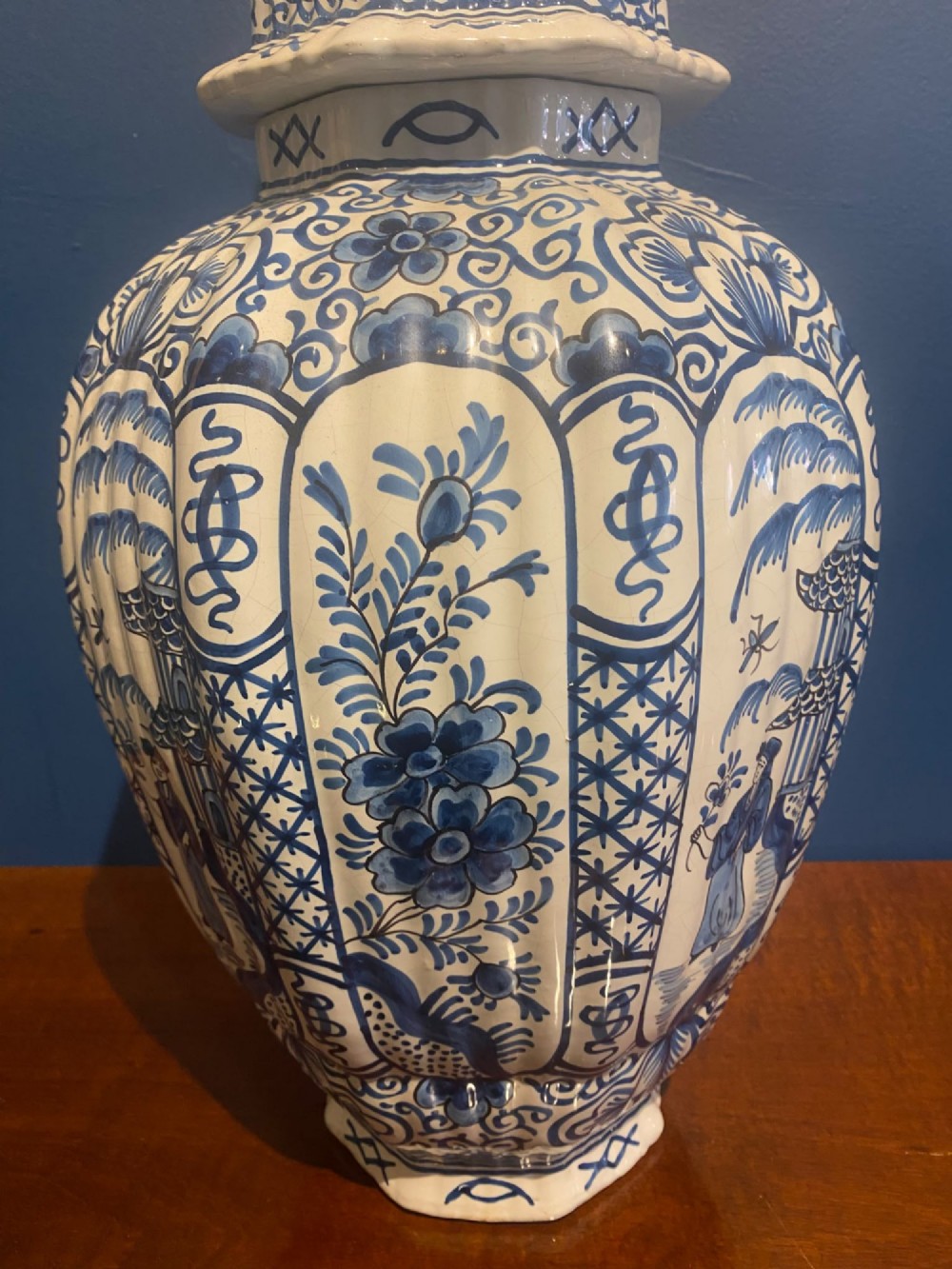 A pair of mid-19th century ribbed blue and white tin-glazed earthenware lidded vases hand-painted with oriental landscapes and topped with seated lion finials. View VI