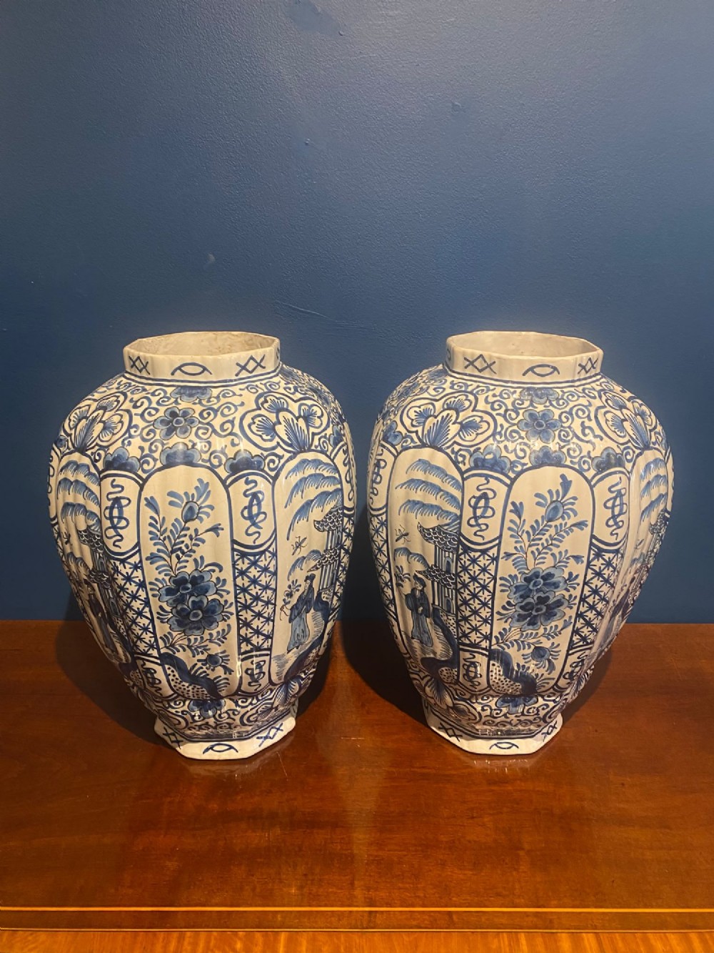 A pair of mid-19th century ribbed blue and white tin-glazed earthenware lidded vases hand-painted with oriental landscapes and topped with seated lion finials. View IX