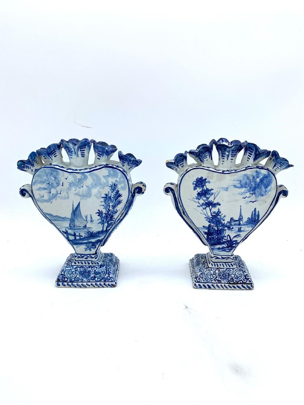 A pair of blue and white heart-shaped ceramic tulipieres featuring multiple spouts and hand-painted Dutch figures in landscape settings. View II