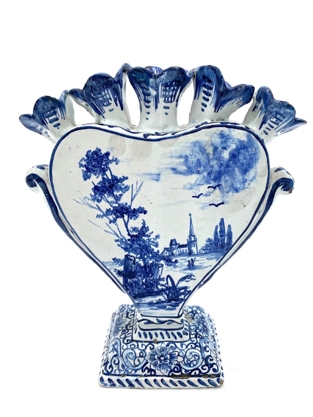 A pair of blue and white heart-shaped ceramic tulipieres featuring multiple spouts and hand-painted Dutch figures in landscape settings. View X