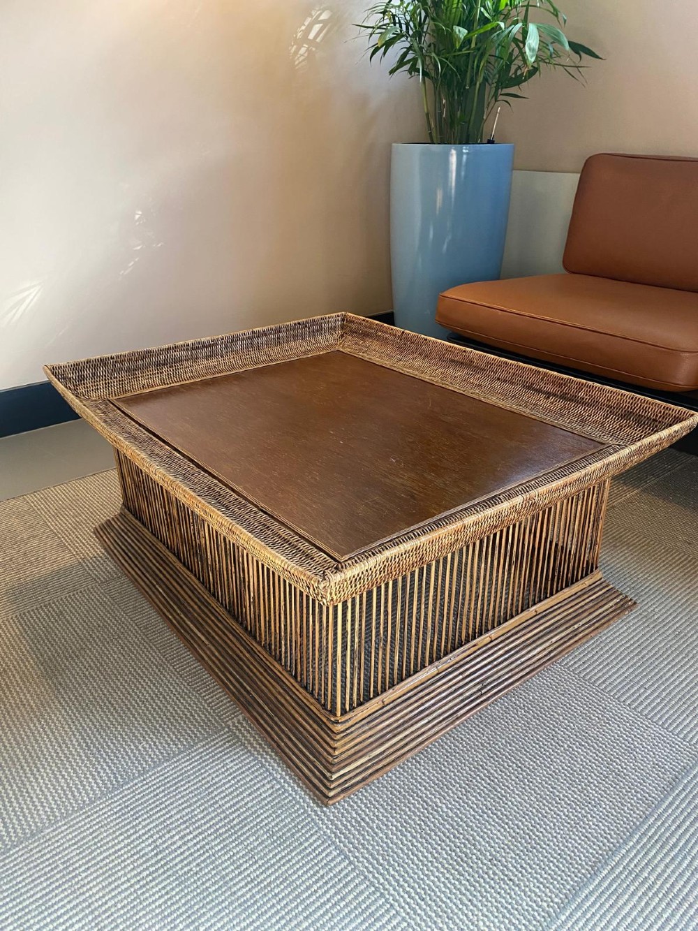 A rectangular warm brown wooden coffee table featuring a recessed top panel surrounded by woven rattan borders and vertical reed slatted sides.