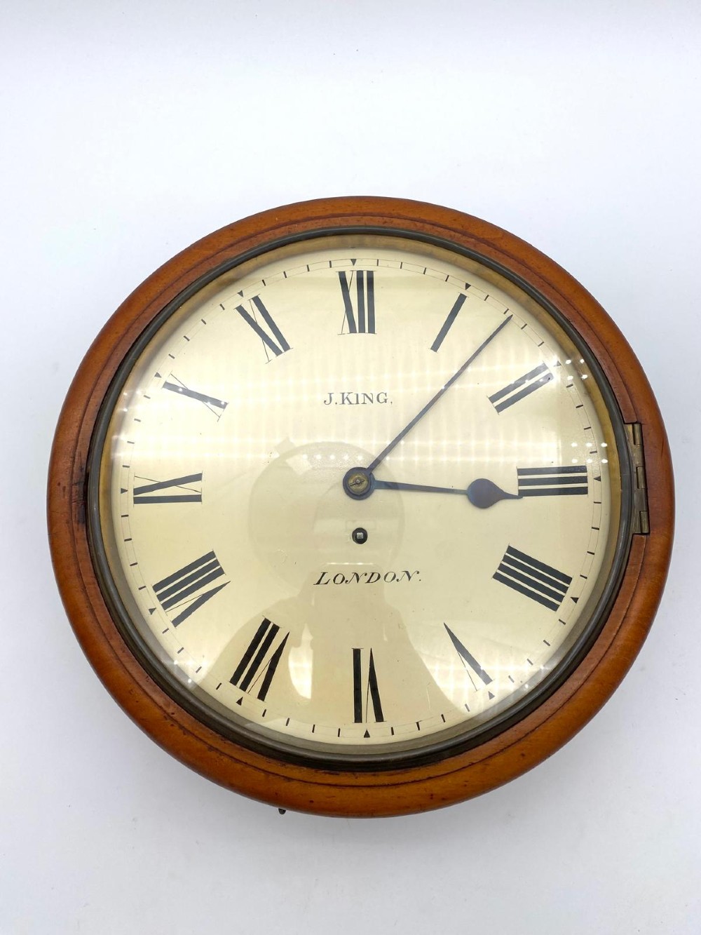 An early Victorian circular mahogany fusee wall clock featuring a cream dial with black Roman numerals and a hinged brass bezel.