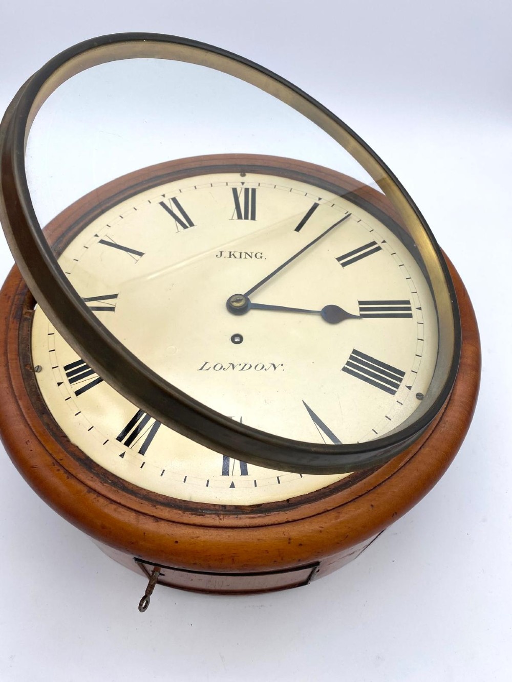 An early Victorian circular mahogany fusee wall clock featuring a cream dial with black Roman numerals and a hinged brass bezel. View V
