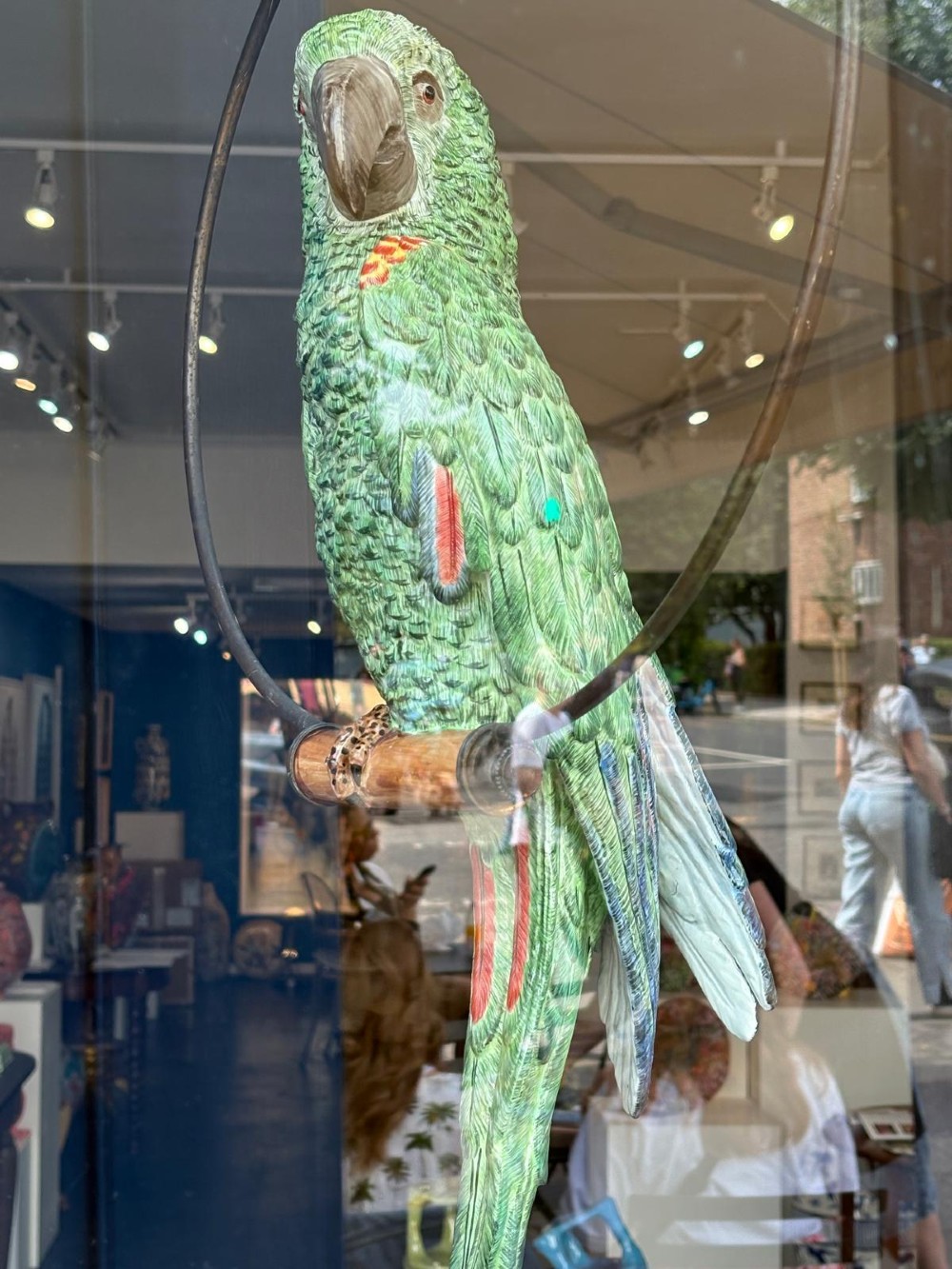 A Victorian green glazed pottery parrot perched on a wooden bar, suspended inside a circular metal hanging hoop. View II