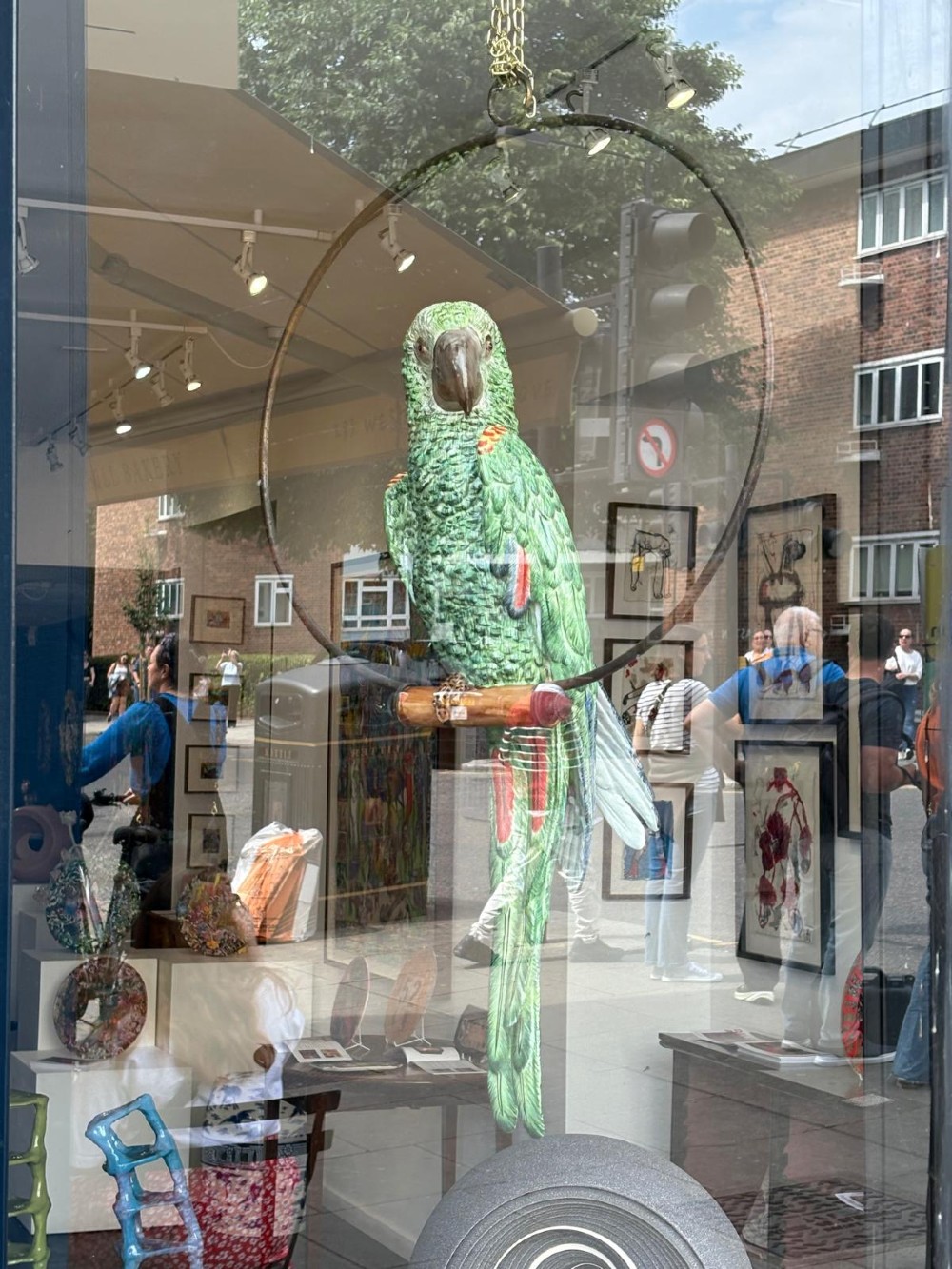 A Victorian green glazed pottery parrot perched on a wooden bar, suspended inside a circular metal hanging hoop. View III