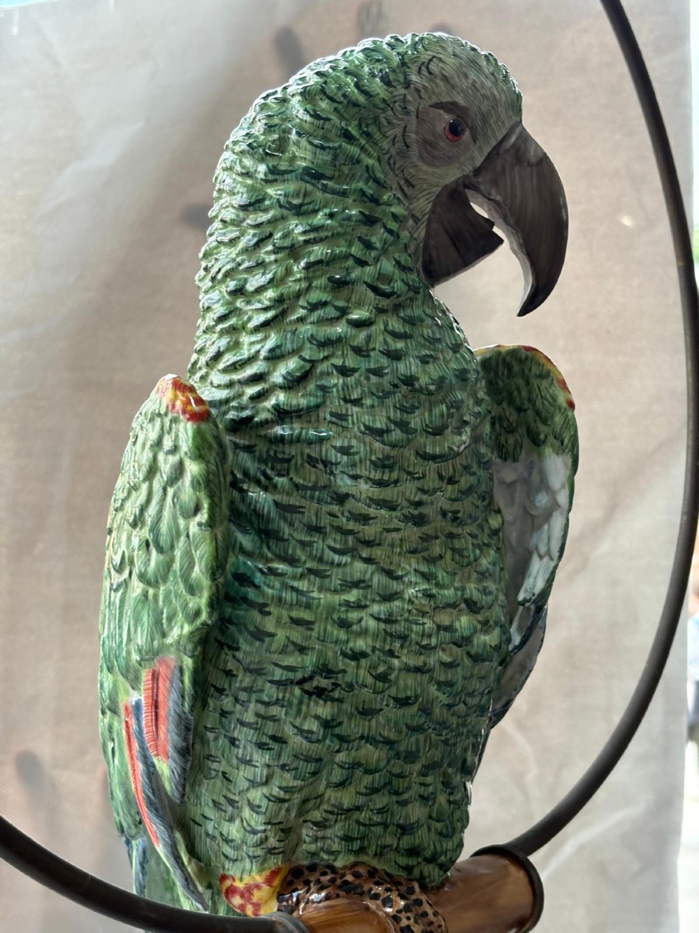 A Victorian green glazed pottery parrot perched on a wooden bar, suspended inside a circular metal hanging hoop. View IV