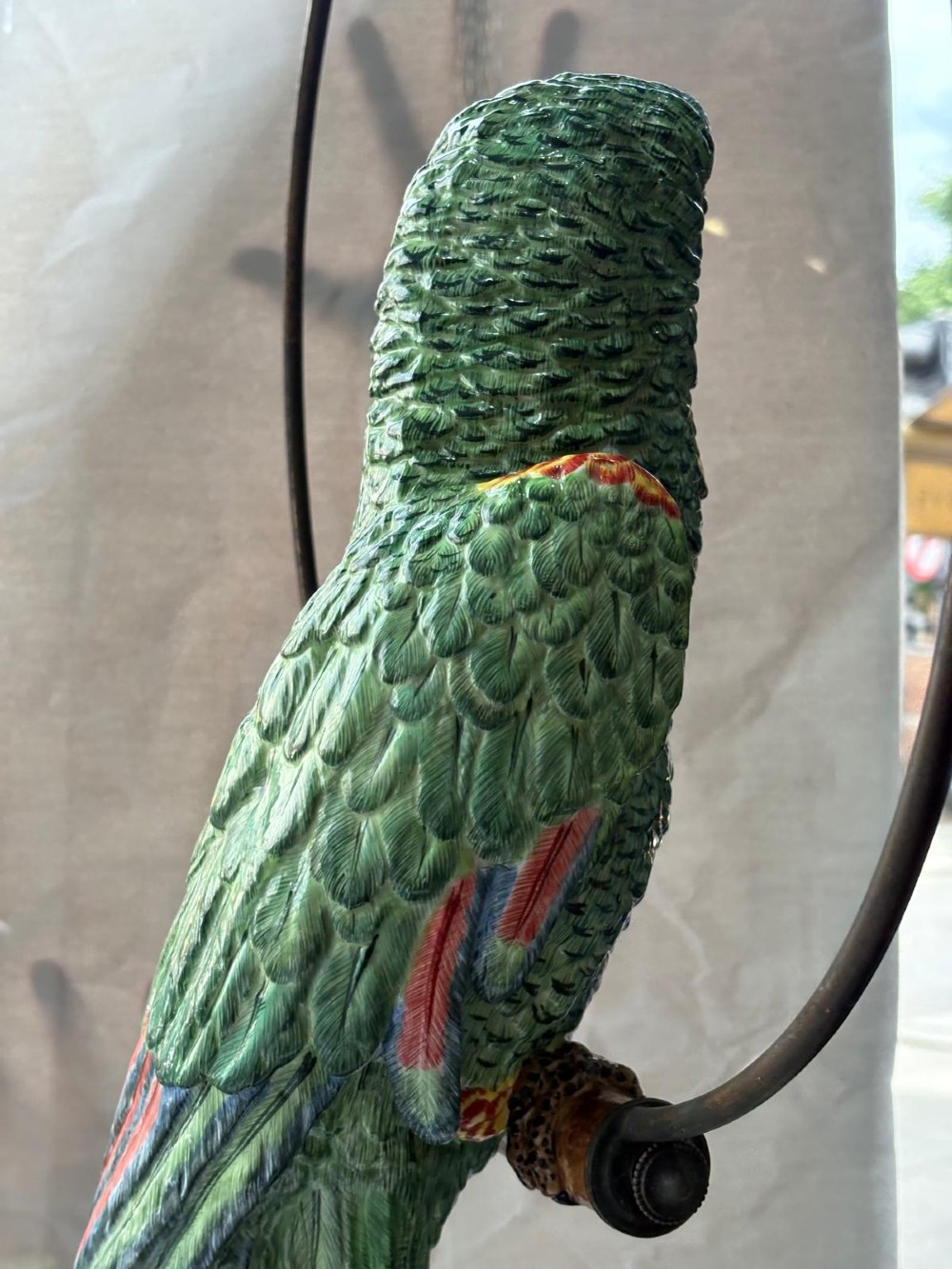 A Victorian green glazed pottery parrot perched on a wooden bar, suspended inside a circular metal hanging hoop. View V