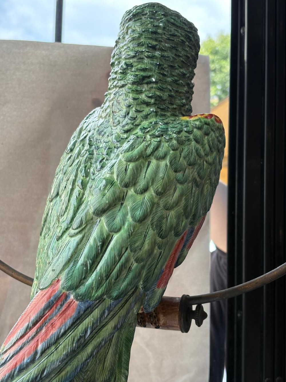 A Victorian green glazed pottery parrot perched on a wooden bar, suspended inside a circular metal hanging hoop. View VI