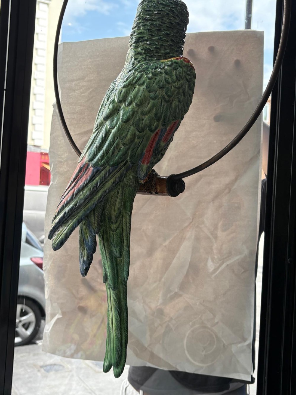 A Victorian green glazed pottery parrot perched on a wooden bar, suspended inside a circular metal hanging hoop. View IX