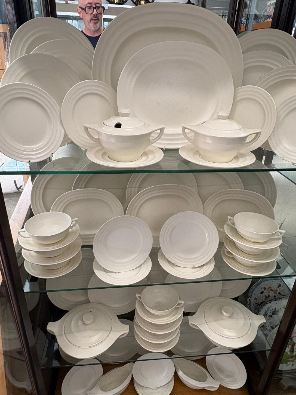 A comprehensive Art Deco off-white ceramic dinner service by Keith Murray for Wedgwood, featuring tiered plates, platters, covered tureens, and soup bowls with ribbed concentric detailing. View II