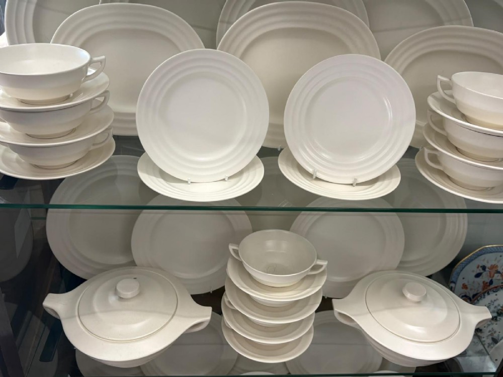 A comprehensive Art Deco off-white ceramic dinner service by Keith Murray for Wedgwood, featuring tiered plates, platters, covered tureens, and soup bowls with ribbed concentric detailing. View III