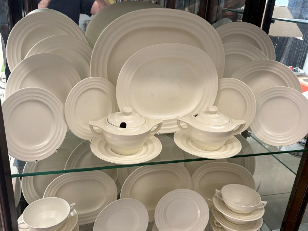 A comprehensive Art Deco off-white ceramic dinner service by Keith Murray for Wedgwood, featuring tiered plates, platters, covered tureens, and soup bowls with ribbed concentric detailing. View IV