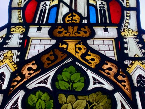 fig 1. An arched Gothic Revival stained glass panel featuring painted architectural spires, foliate patterns, and lead cames in red, green, yellow, and clear glass.