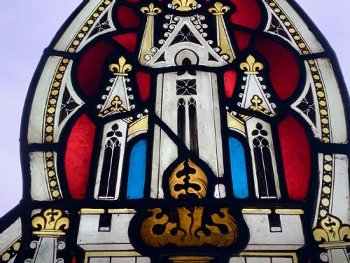 fig 2. An arched Gothic Revival stained glass panel featuring painted architectural spires, foliate patterns, and lead cames in red, green, yellow, and clear glass.