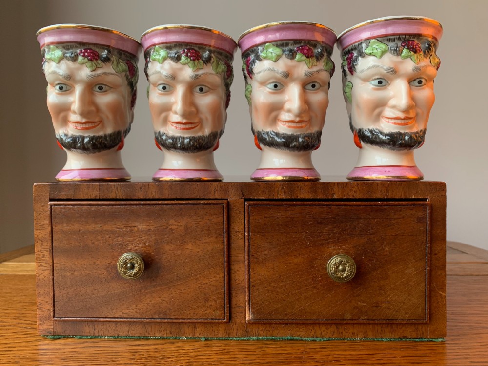 A set of four Victorian Staffordshire ceramic wine cups moulded in the form of bearded satyr faces with grapevine crowns and pink gilded rims.