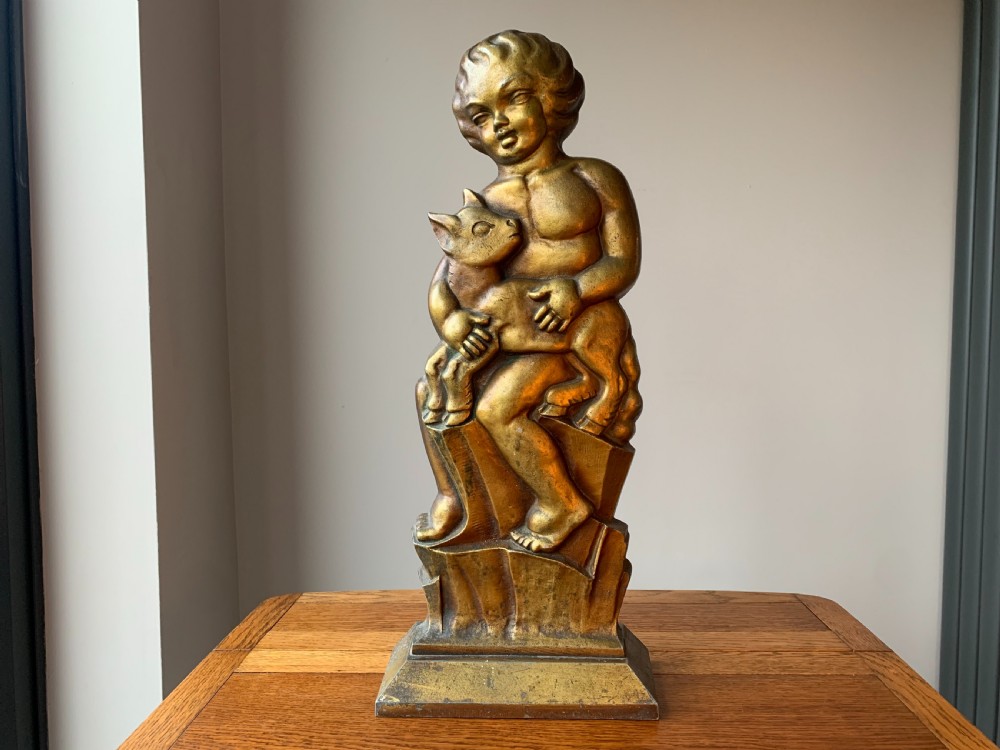 A gilded brass Art Deco sculptural companion set piece depicting a child holding a lamb atop a stepped geometric base.