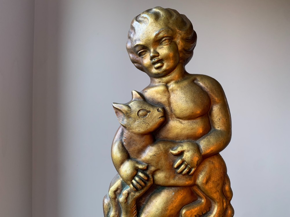 A gilded brass Art Deco sculptural companion set piece depicting a child holding a lamb atop a stepped geometric base. View X