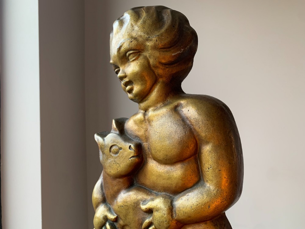 A gilded brass Art Deco sculptural companion set piece depicting a child holding a lamb atop a stepped geometric base. View XV
