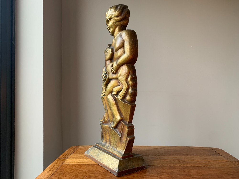 A gilded brass Art Deco sculptural companion set piece depicting a child holding a lamb atop a stepped geometric base. View XVI