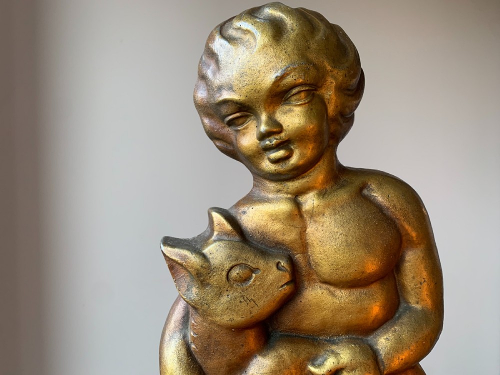 A gilded brass Art Deco sculptural companion set piece depicting a child holding a lamb atop a stepped geometric base. View XVIII