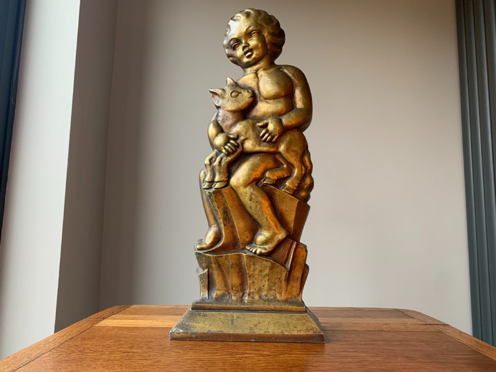A gilded brass Art Deco sculptural companion set piece depicting a child holding a lamb atop a stepped geometric base. View XIX