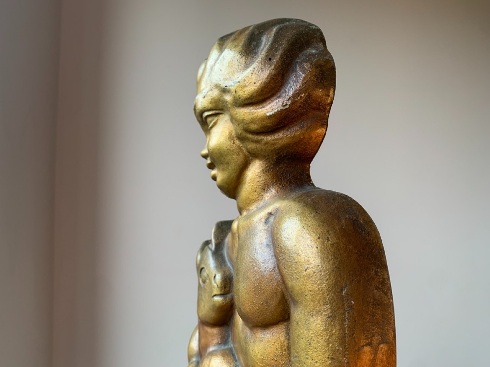 A gilded brass Art Deco sculptural companion set piece depicting a child holding a lamb atop a stepped geometric base. View XX