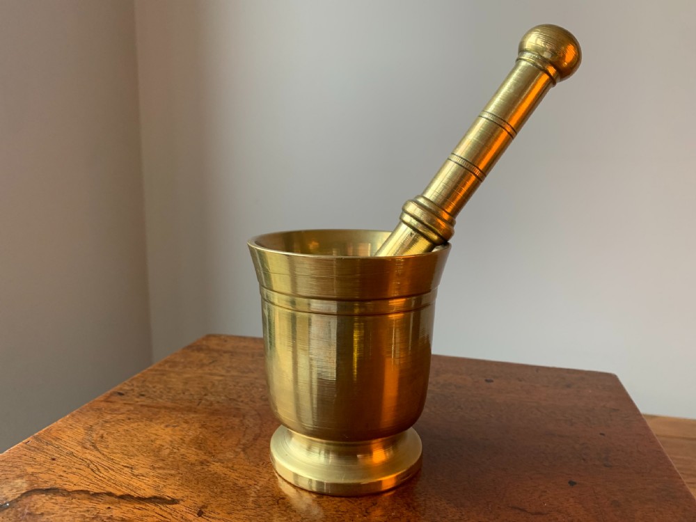 A heavy cast brass mortar with turned incised rings around the body, accompanied by a matching solid brass pestle.