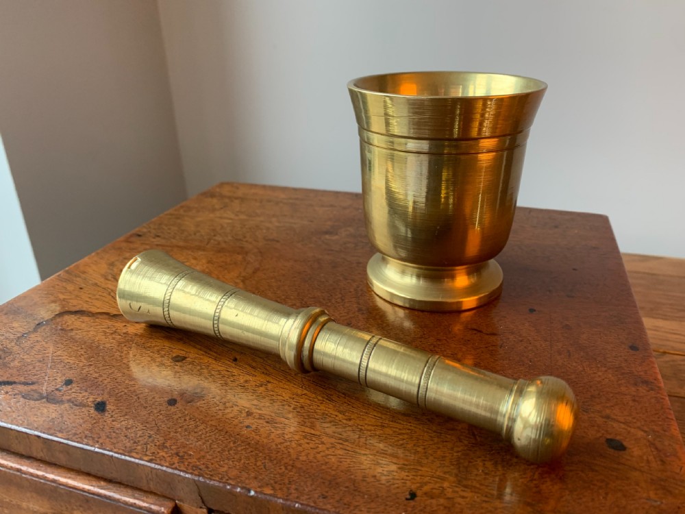 A heavy cast brass mortar with turned incised rings around the body, accompanied by a matching solid brass pestle. View II