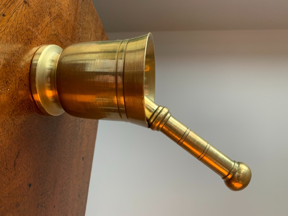 A heavy cast brass mortar with turned incised rings around the body, accompanied by a matching solid brass pestle. View III