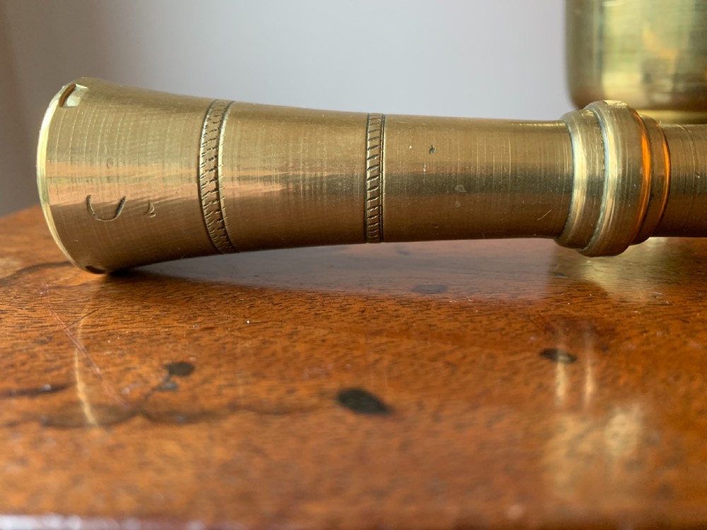 A heavy cast brass mortar with turned incised rings around the body, accompanied by a matching solid brass pestle. View IV