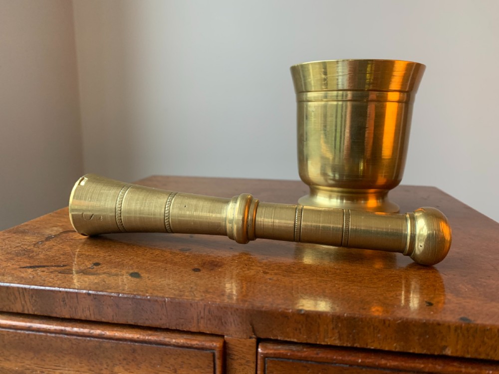 A heavy cast brass mortar with turned incised rings around the body, accompanied by a matching solid brass pestle. View VI