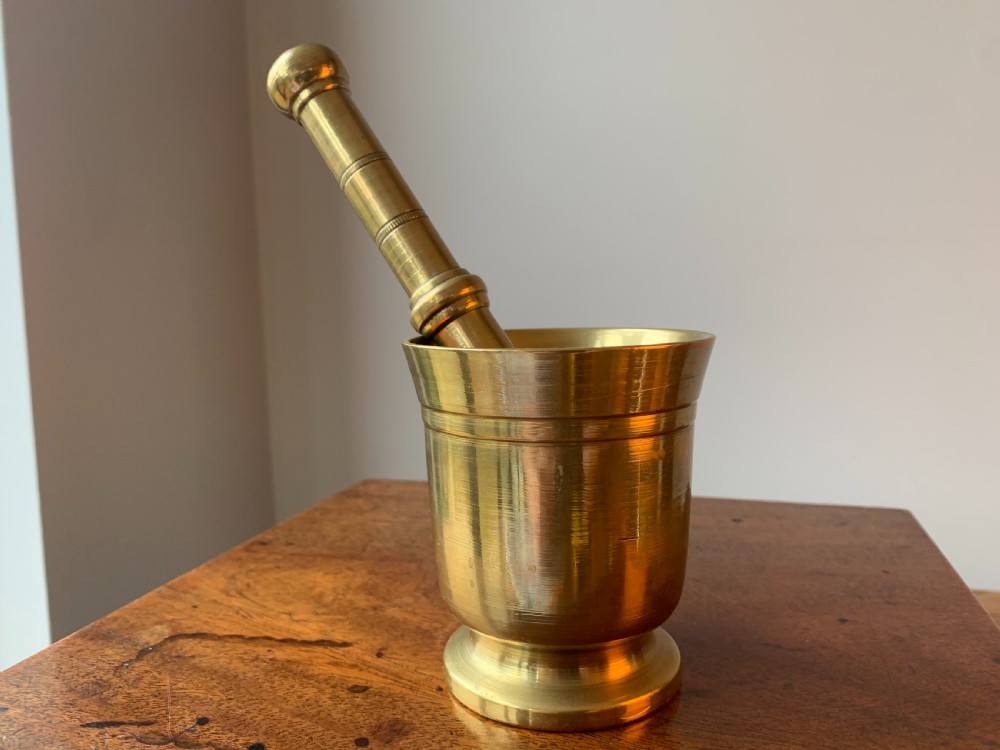 A heavy cast brass mortar with turned incised rings around the body, accompanied by a matching solid brass pestle. View X