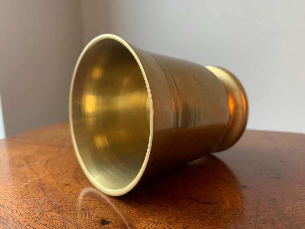 A heavy cast brass mortar with turned incised rings around the body, accompanied by a matching solid brass pestle. View XII