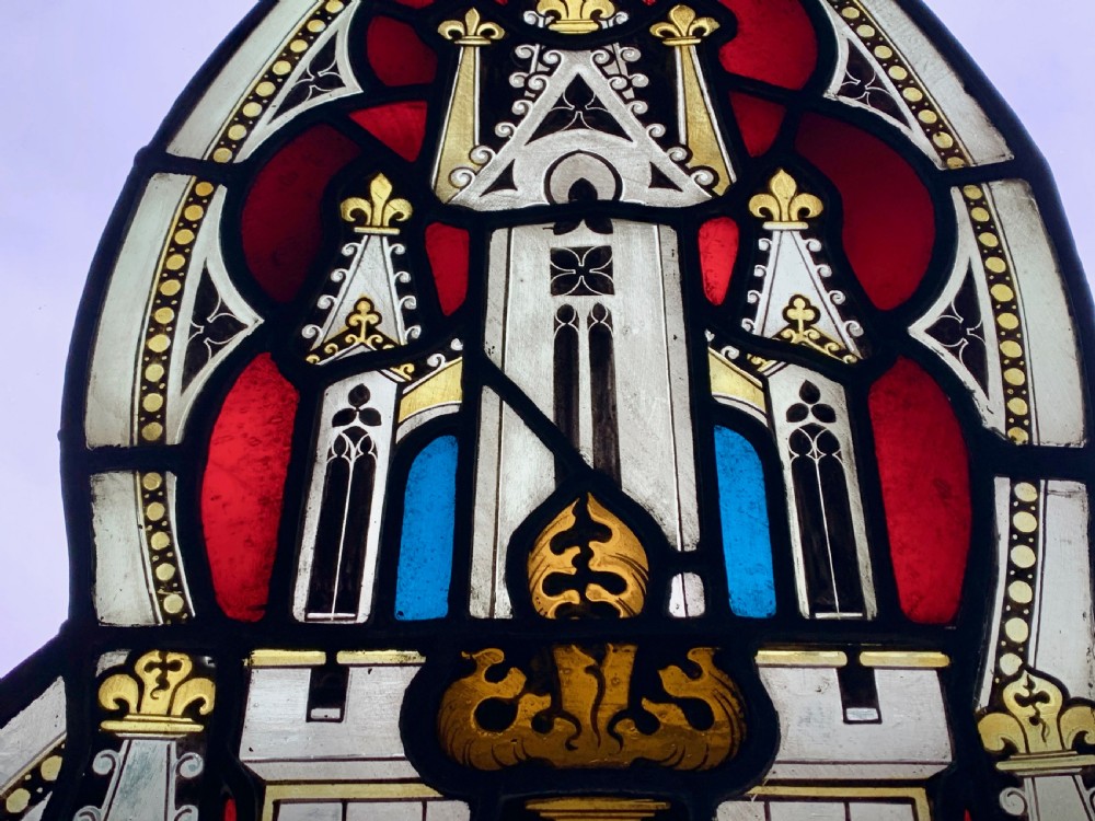 An arched Gothic Revival stained glass panel featuring painted architectural spires, foliate patterns, and lead cames in red, green, yellow, and clear glass. View III