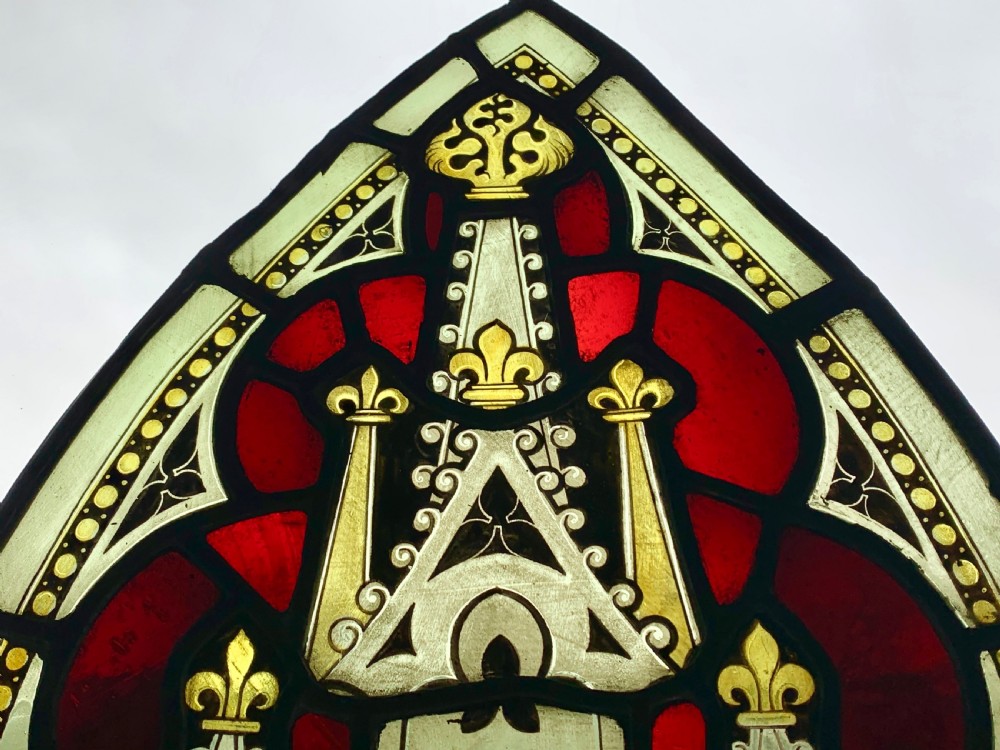 An arched Gothic Revival stained glass panel featuring painted architectural spires, foliate patterns, and lead cames in red, green, yellow, and clear glass. View IV
