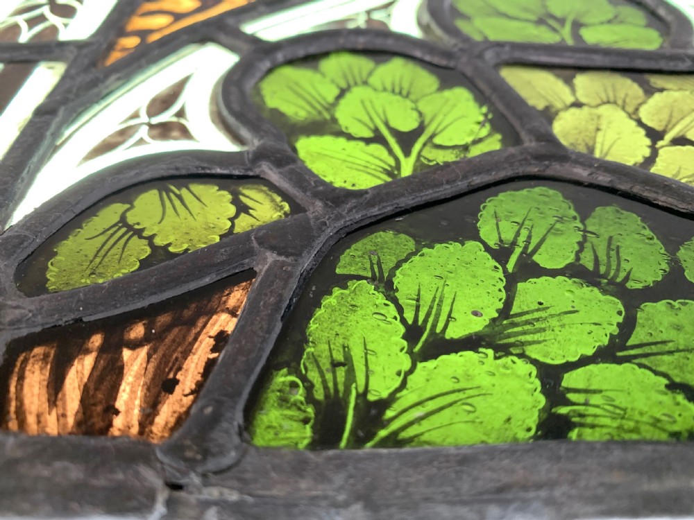 An arched Gothic Revival stained glass panel featuring painted architectural spires, foliate patterns, and lead cames in red, green, yellow, and clear glass. View VI